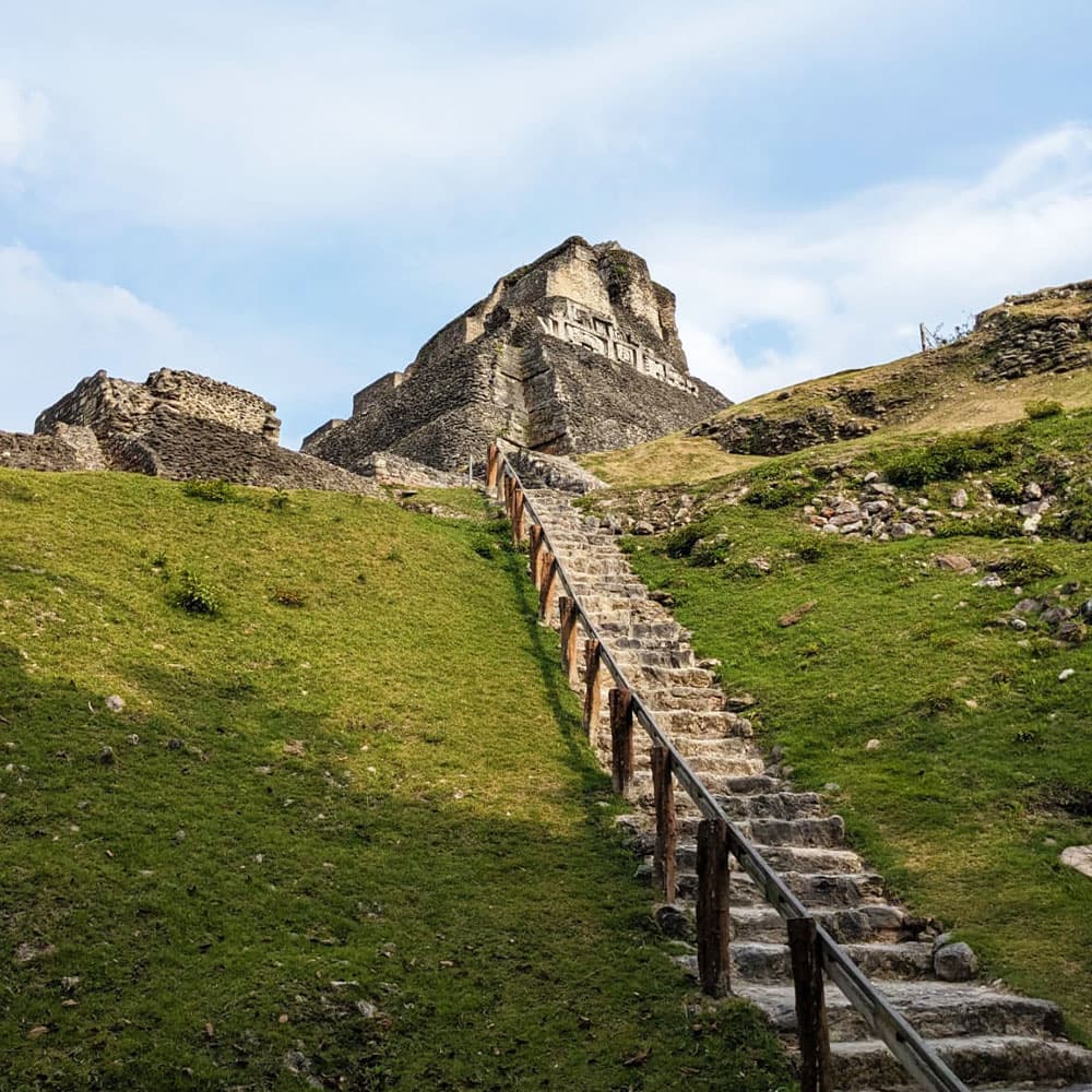 A stone staircase leads up a grassy hill to ancient ruins under a blue sky.