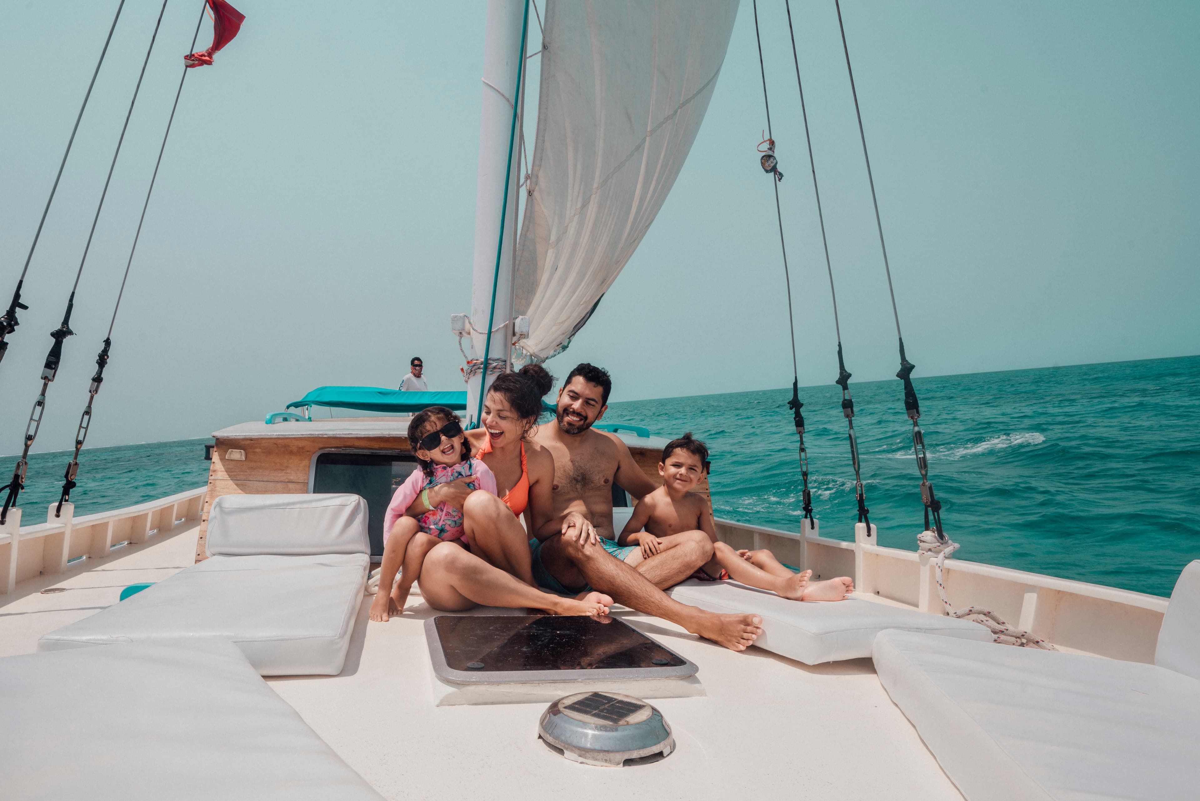 A family enjoys a sunny day on a sailboat, smiling and relaxing by the ocean.