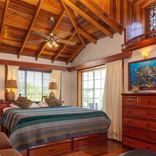 A cozy bedroom featuring a wooden ceiling, a striped bedspread, and large windows with natural light.