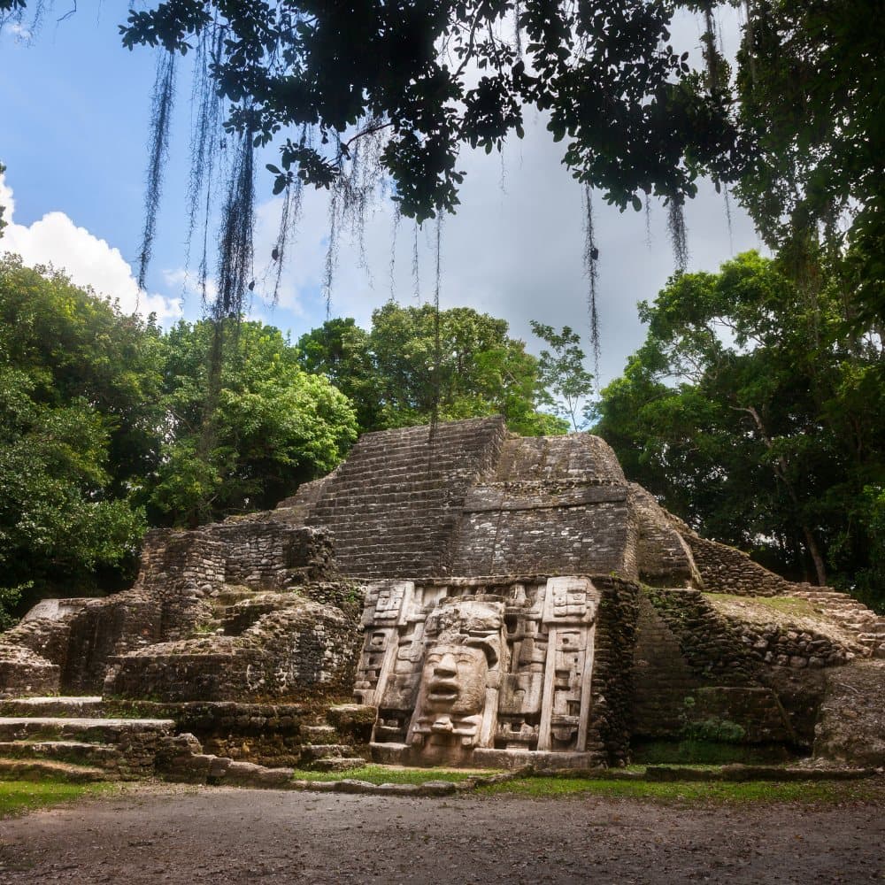 Ancient Mayan ruins with a sculpted stone face, surrounded by lush greenery.