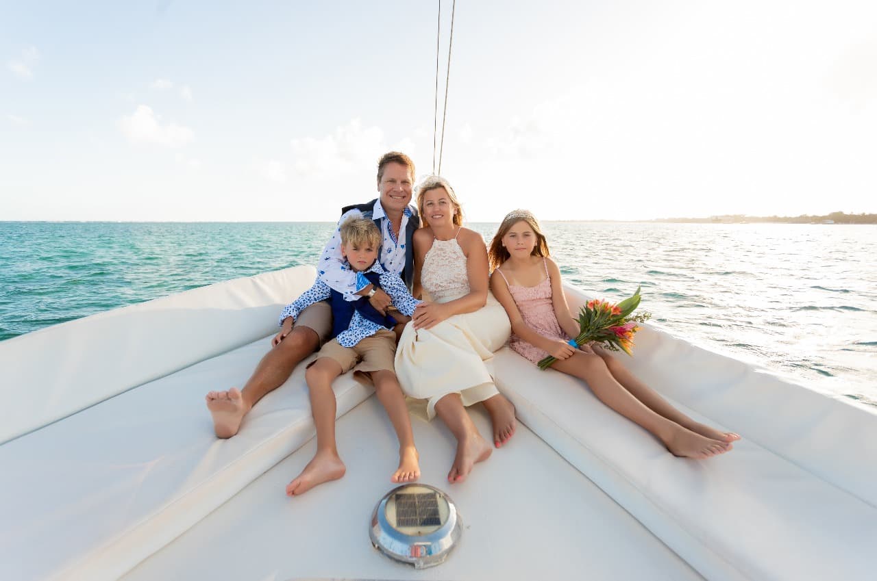 A family sitting together on the bow of a sailboat, smiling at the camera.