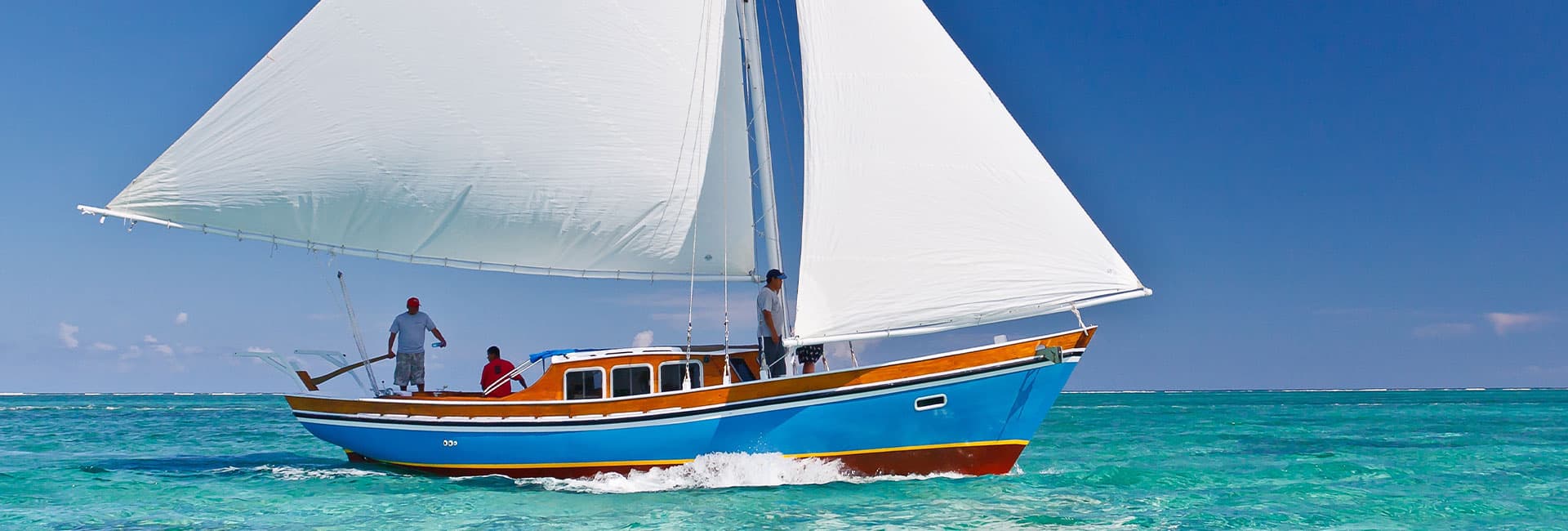 A colorful sailing boat glides over turquoise waters under a clear blue sky.