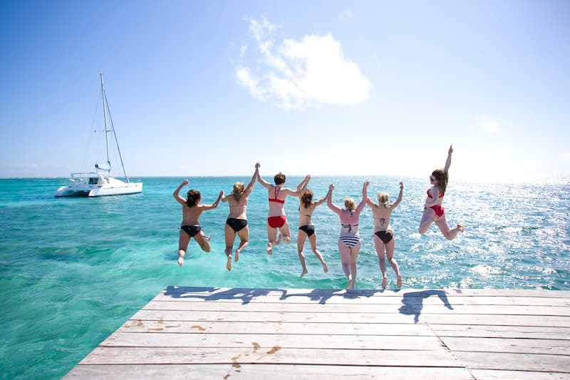 A group of women jumps off a dock into clear blue water on a sunny day.