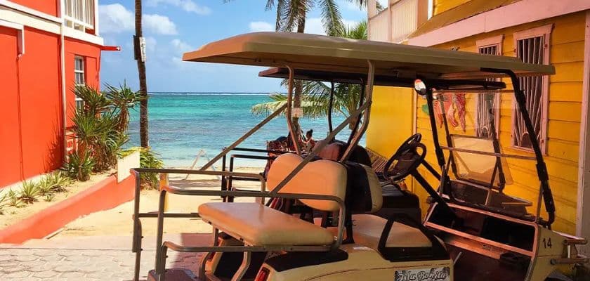 A golf cart parked near colorful buildings with a beach and ocean in the background.
