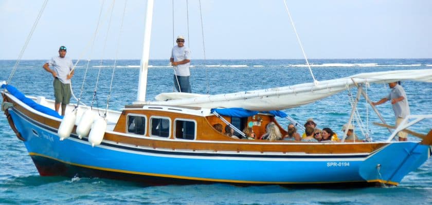 A group of people enjoys a boat ride on a blue wooden sailboat in the ocean.