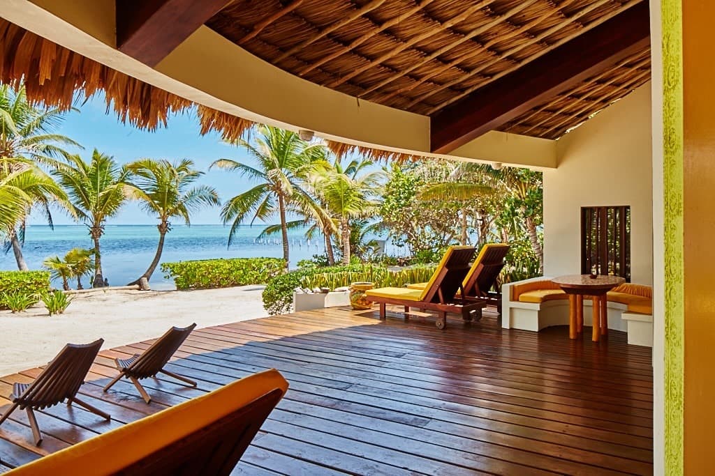 A tropical beachfront view from a wooden deck with lounge chairs.