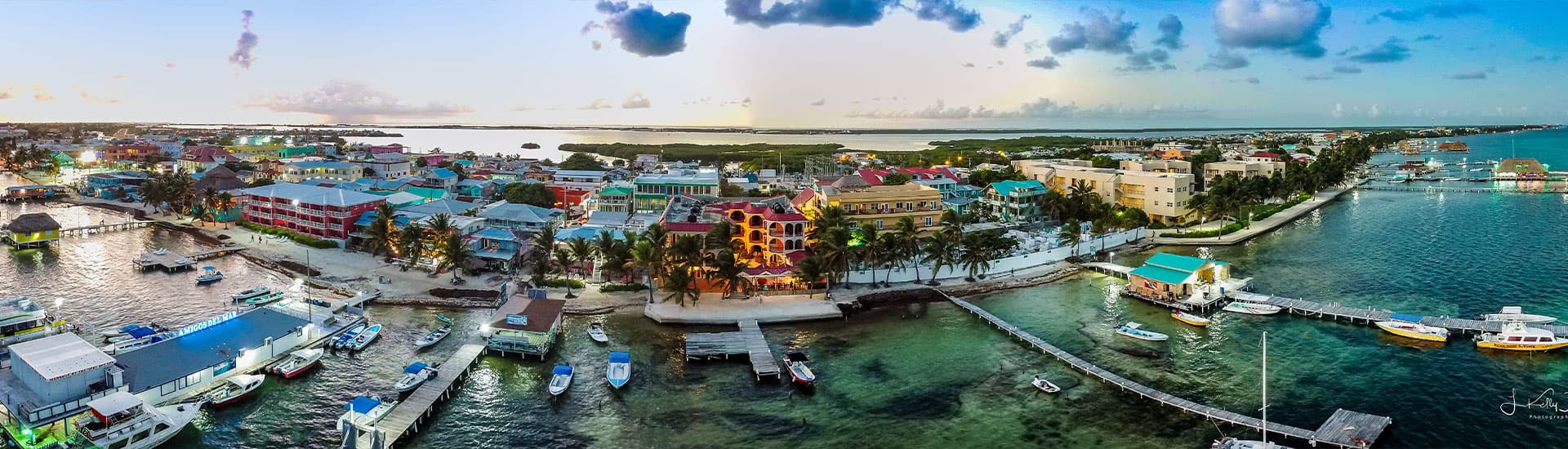 Aerial view of a vibrant coastal town with colorful buildings and boats along the waterfront at sunset.