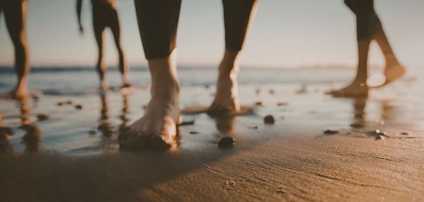 Feet walking along a sandy beach with gentle waves in the background.