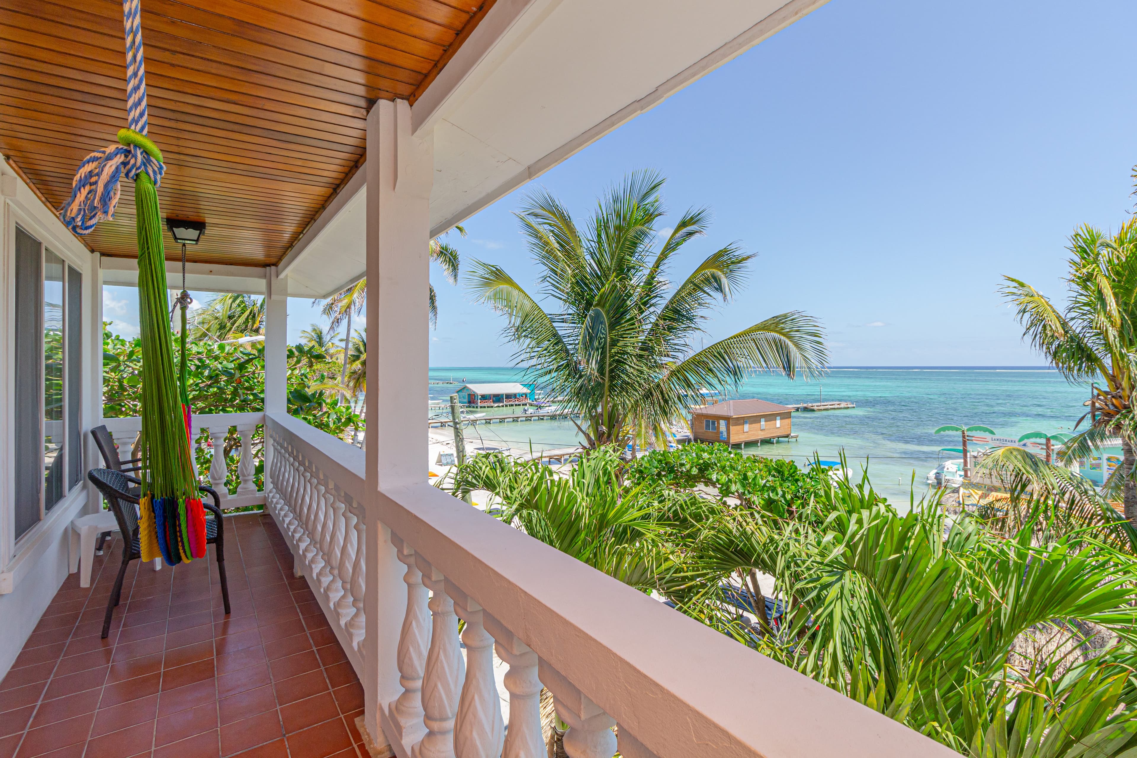 A vibrant balcony with a colorful hammock overlooks a tropical beach and turquoise water.