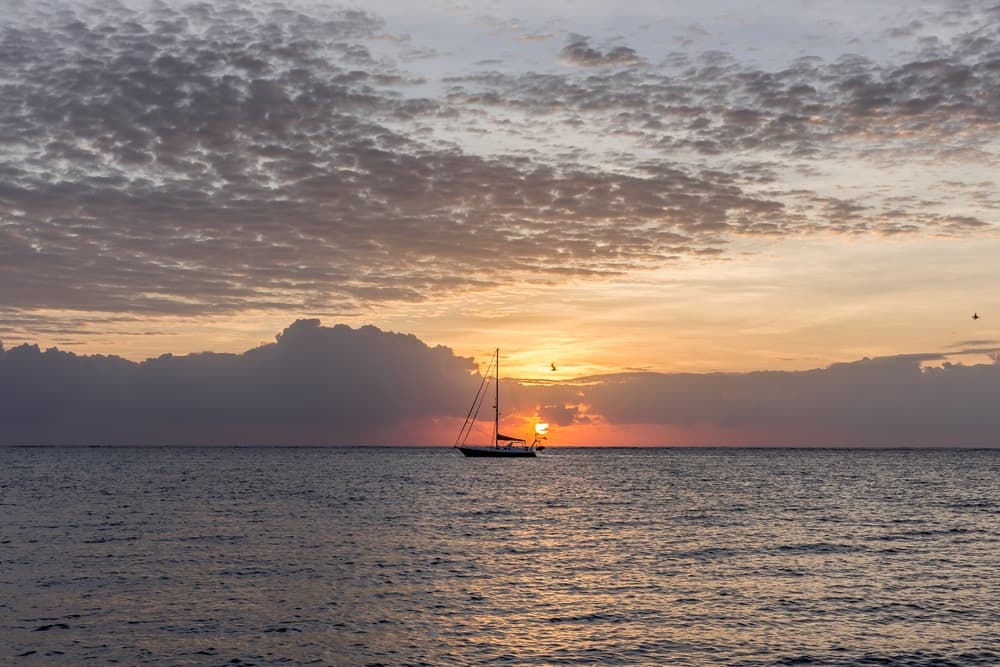 A sailboat is silhouetted against a vibrant sunset over the ocean.