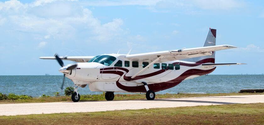A white and maroon airplane is parked by the shore with the ocean in the background.