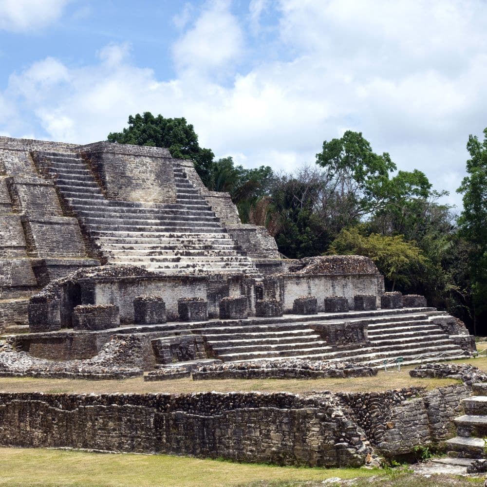 Ancient stone pyramid with tiered steps set against a blue sky and greenery.