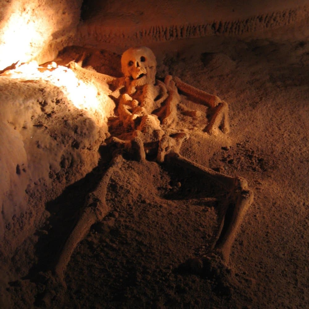 A human skeleton partially uncovered in sandy earth, illuminated by soft lighting.