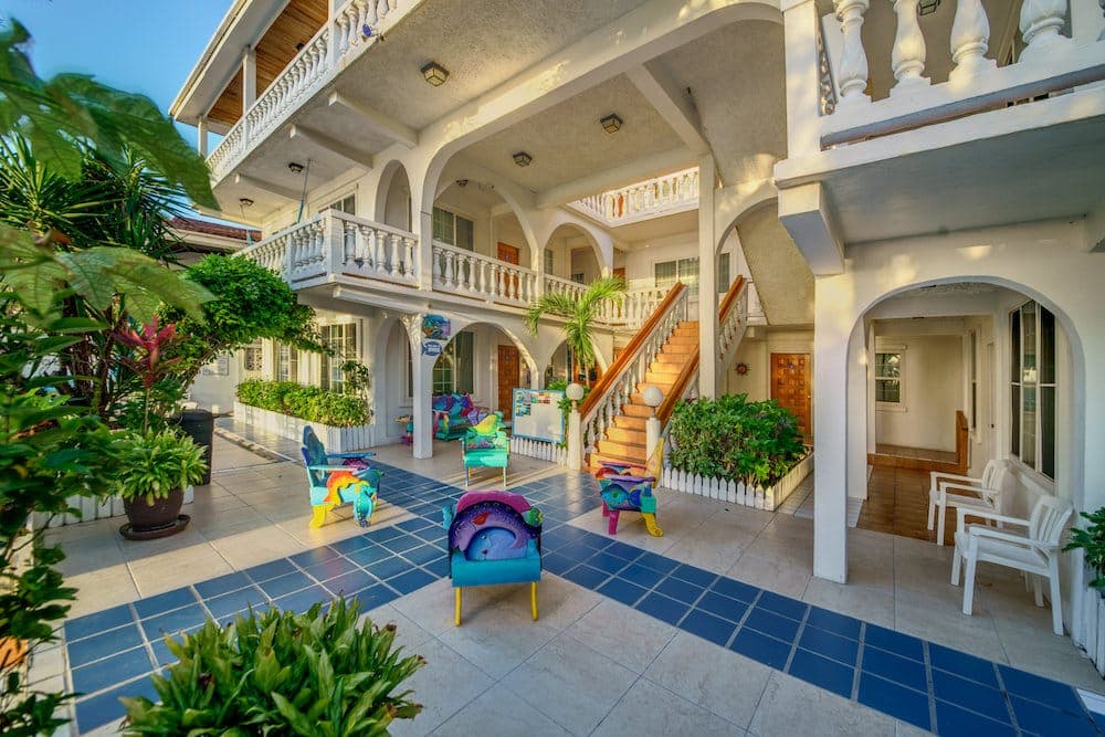 A vibrant courtyard featuring colorful chairs, lush plants, and a staircase leading to upper levels of a building.