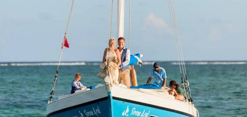 A bride and groom pose on a sailboat surrounded by family in a tropical setting.