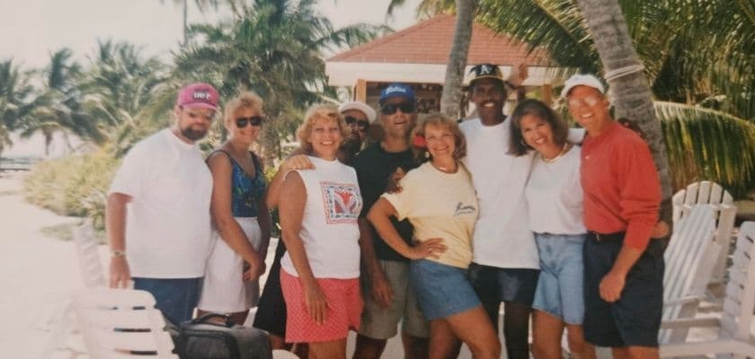 A group of eight people posing together in a tropical setting with palm trees in the background.