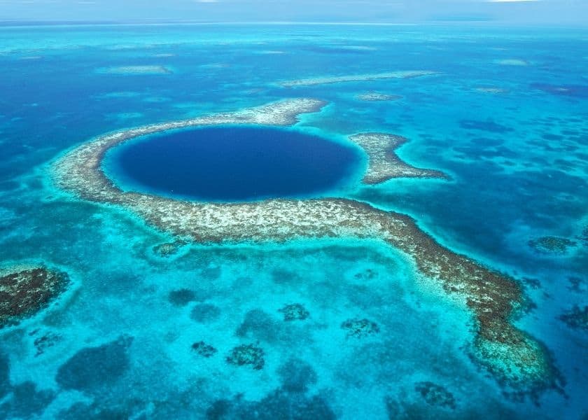 Aerial view of the Great Blue Hole, a circular marine sinkhole surrounded by turquoise waters and coral reefs. Aerial view of the Great Blue Hole, a circular marine sinkhole surrounded by turquoise waters and coral reefs.
