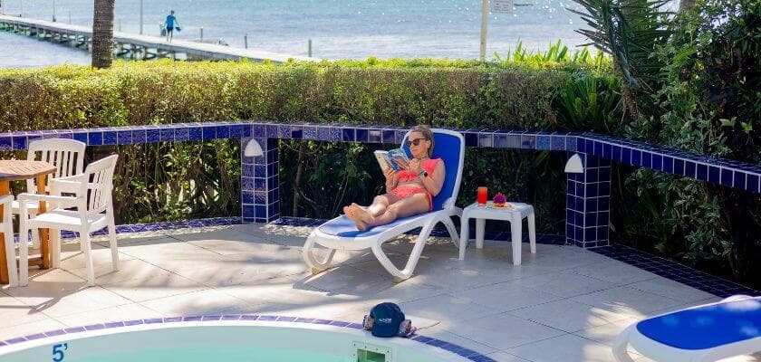 A woman in a pink bikini relaxes on a lounge chair by a pool, reading a book.