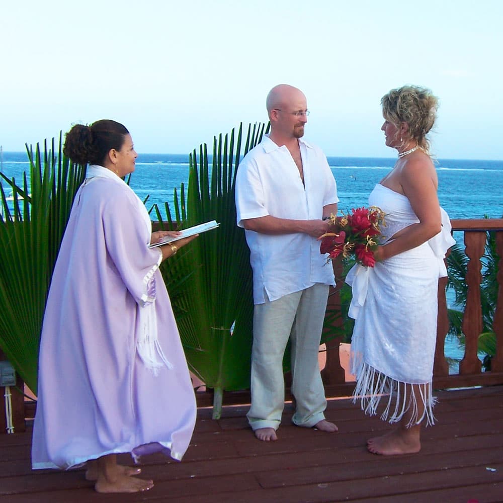 A couple exchanges vows during a beachfront wedding ceremony, accompanied by an officiant.
