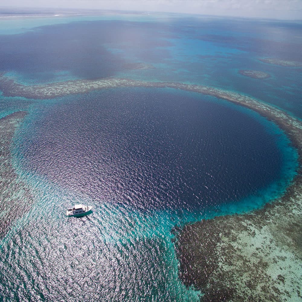 Aerial view of a circular blue hole in the ocean with a boat nearby.