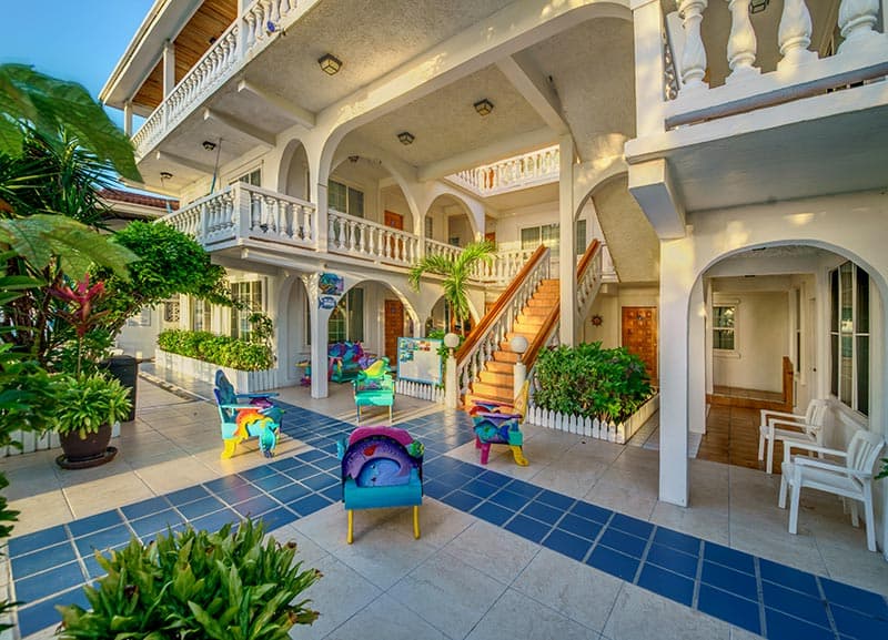 A colorful courtyard of a building featuring vibrant chairs, tropical plants, and a staircase.