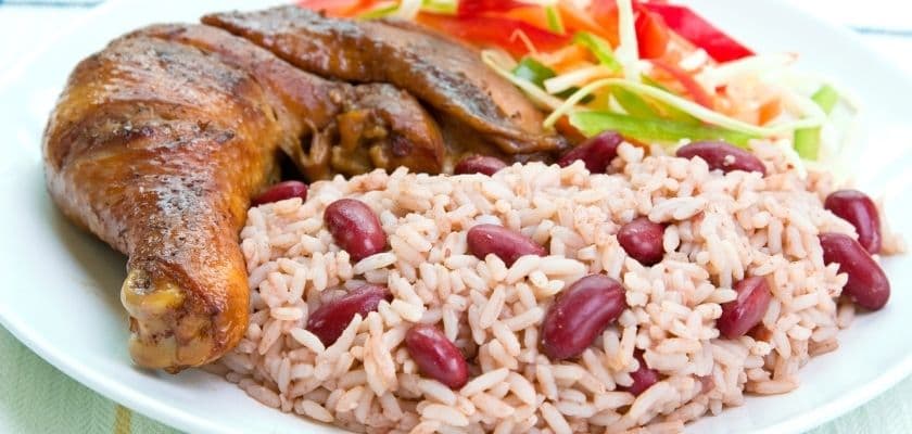 Plate of grilled chicken served with rice and beans, accompanied by a fresh vegetable salad.