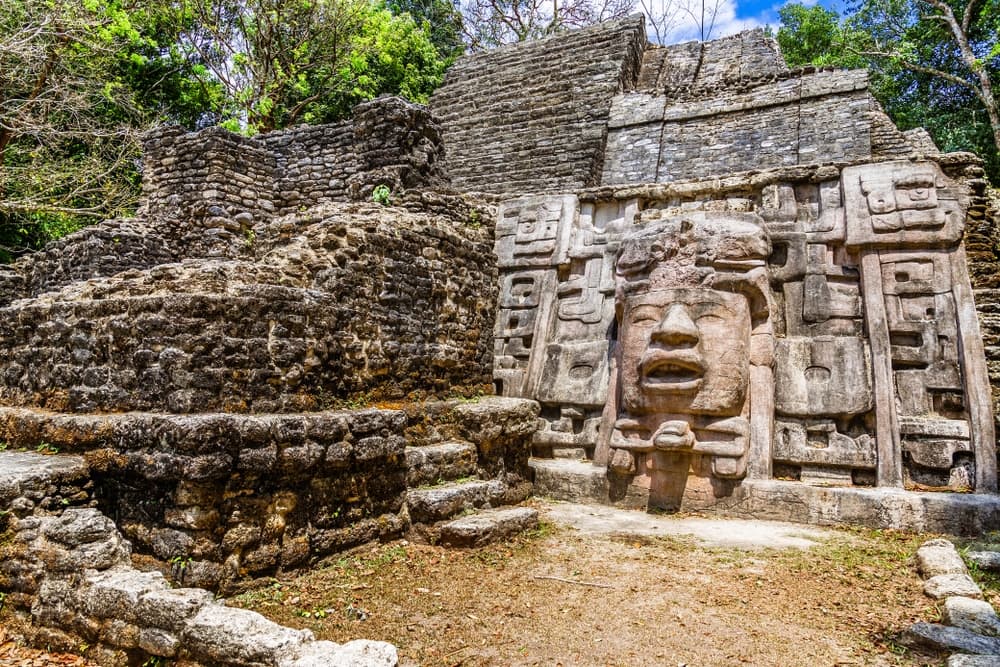 Ancient stone ruins with a carved face amidst lush greenery.