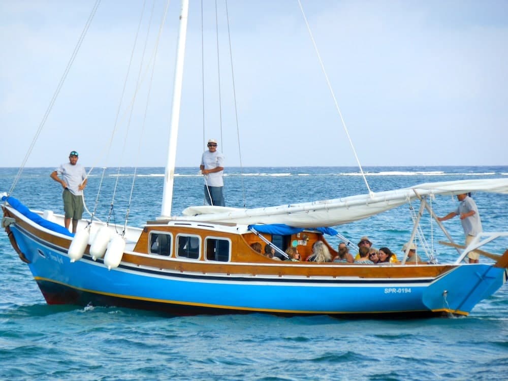 A large blue wooden boat with several people on board sailing in calm waters.