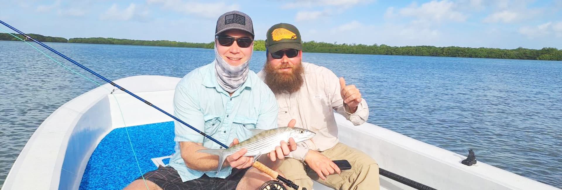 Two men in a boat proudly display a caught fish against a scenic water backdrop.