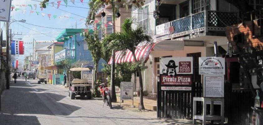A colorful street lined with shops and palm trees, featuring a sign for Pirate Pizza.