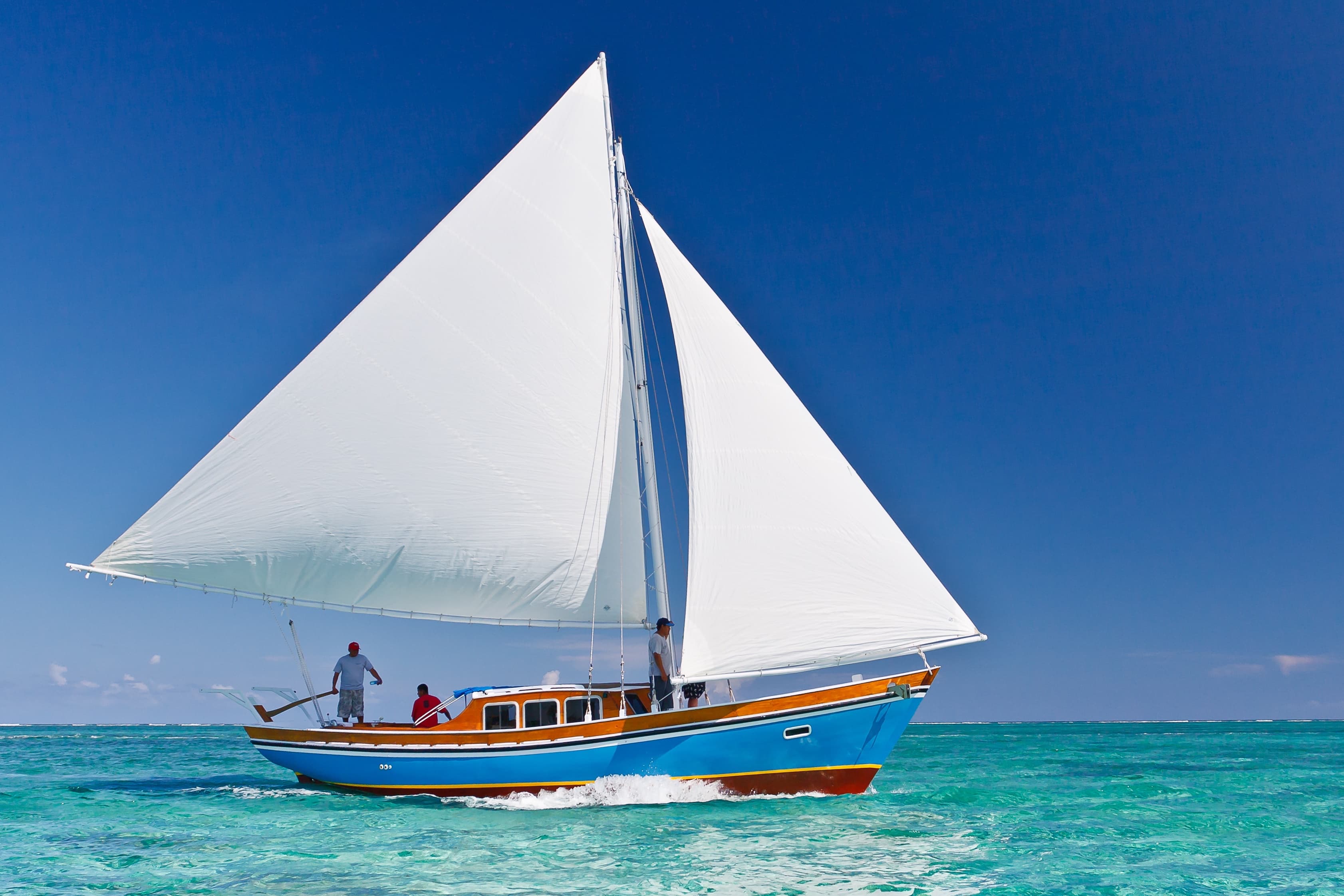 A colorful sailing boat glides across clear turquoise waters under a bright blue sky.
