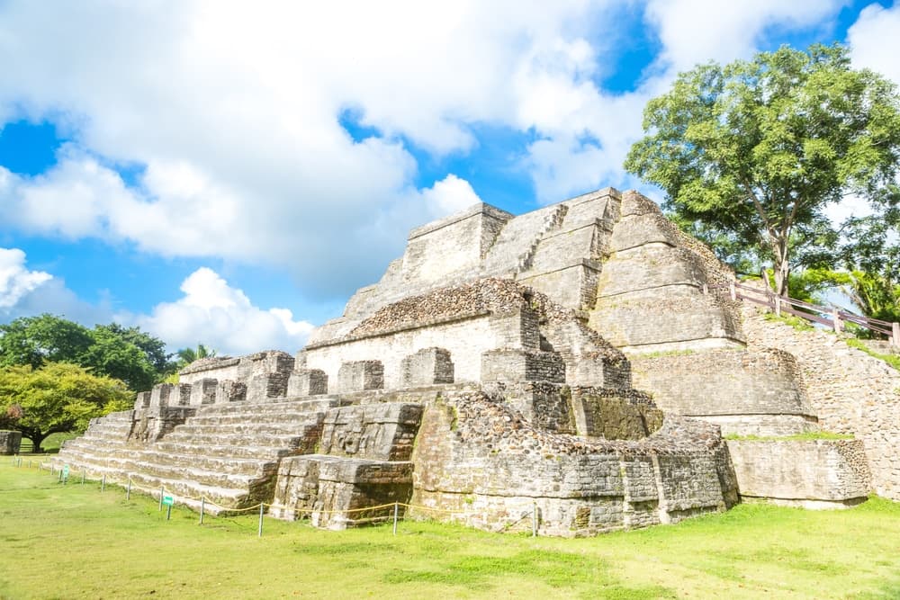 Ancient stone pyramid surrounded by greenery under a bright blue sky.
