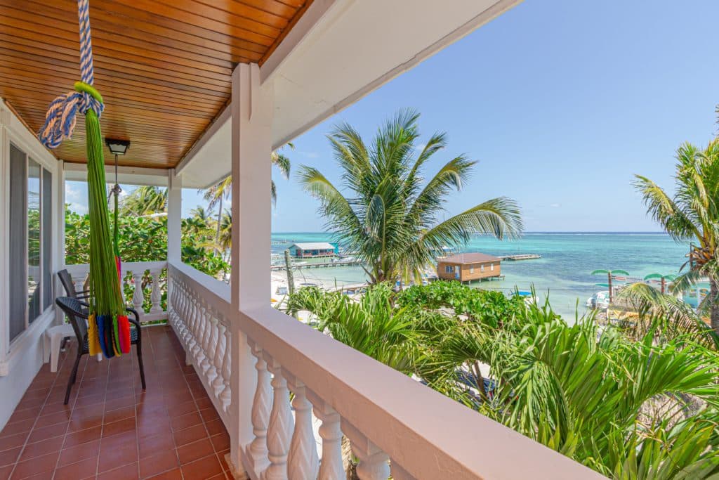 A view from a balcony overlooking the ocean, with palm trees and a hammock.