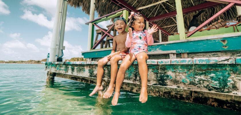 Two children sitting on a wooden dock, playfully splashing their feet in the water.
