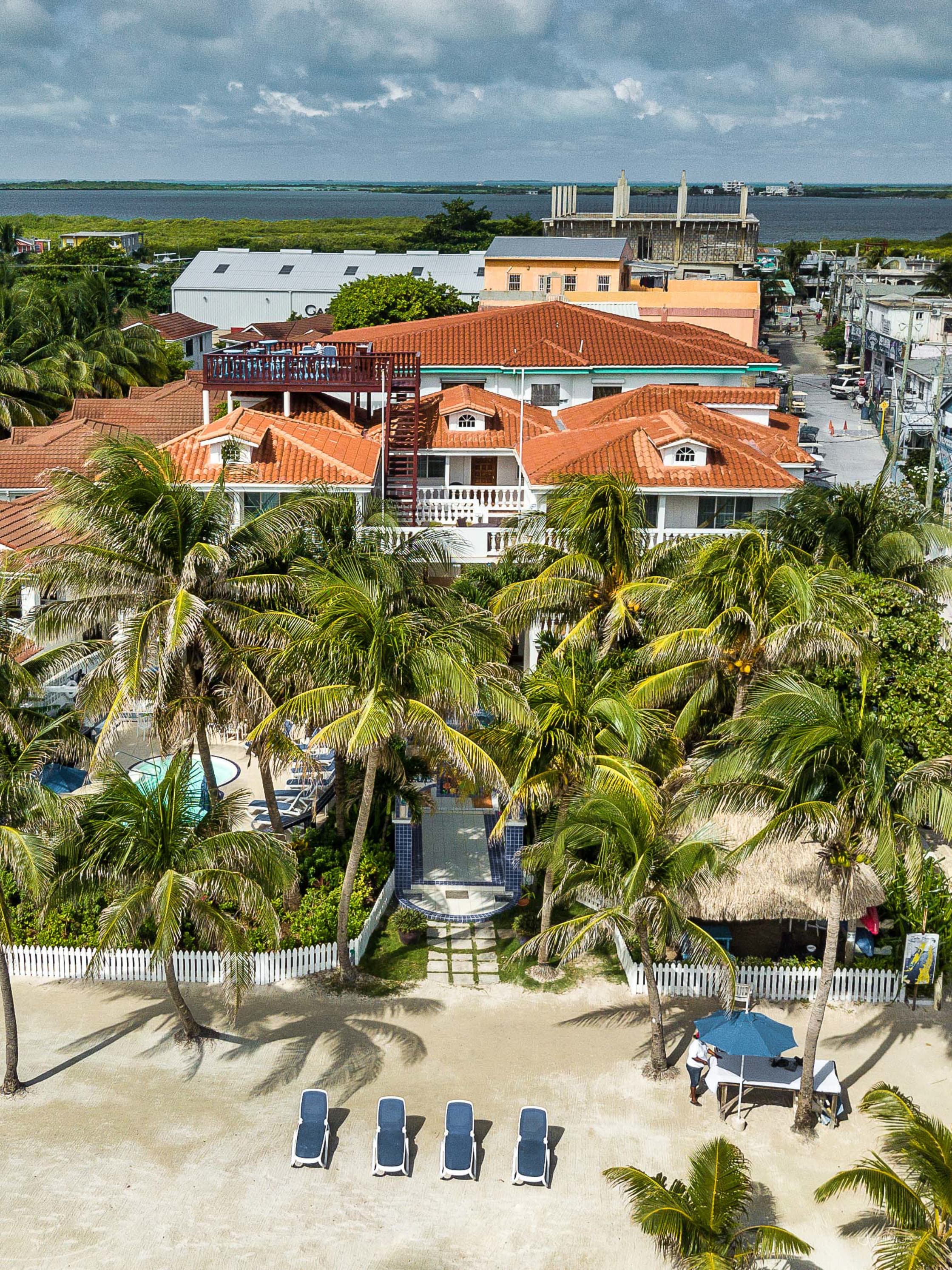 Aerial view of a beachfront hotel with palm trees and a pool, overlooking a blue lagoon.
