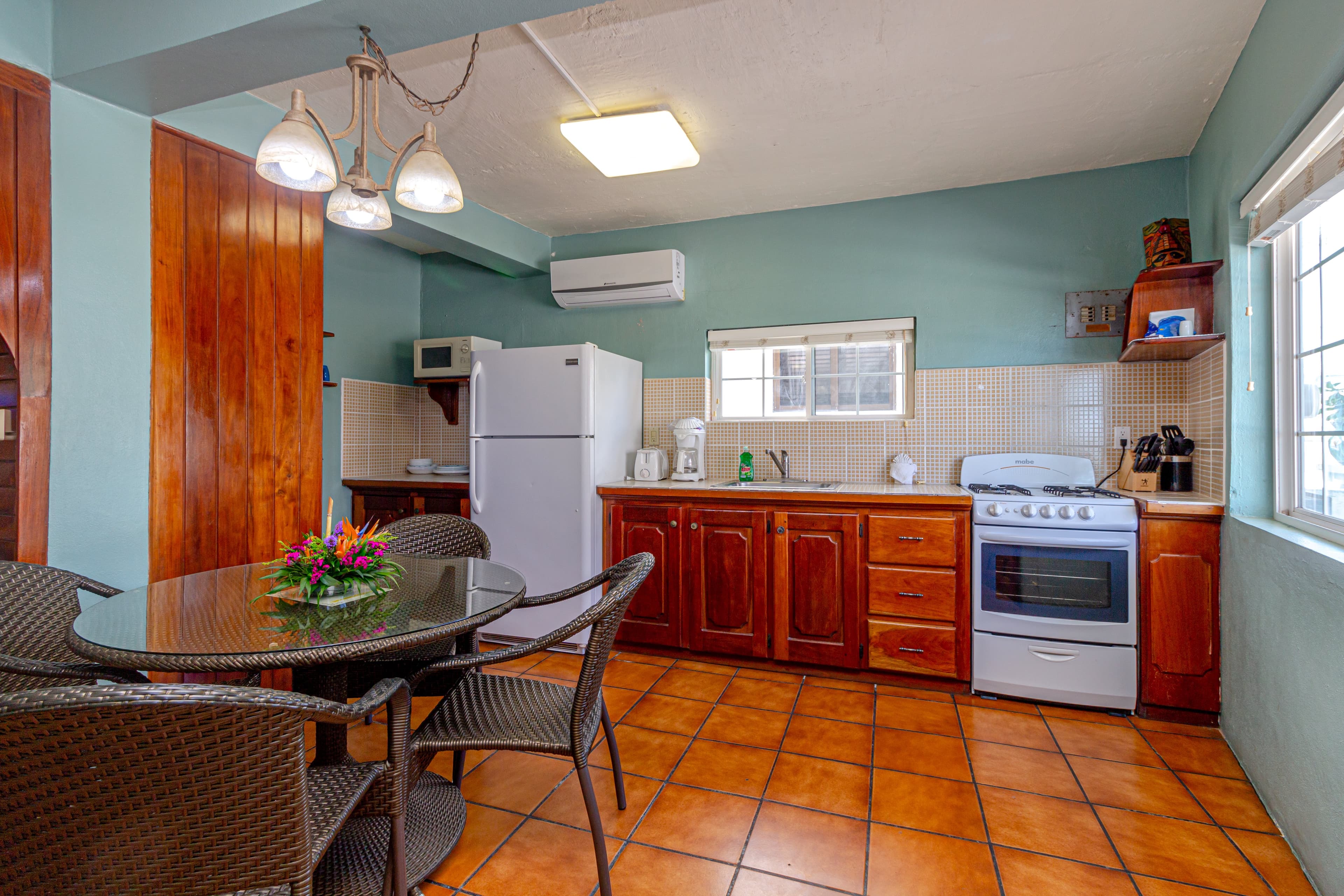 A dining area with a round table and chairs next to a compact kitchenette with white appliances and wooden cabinets.
