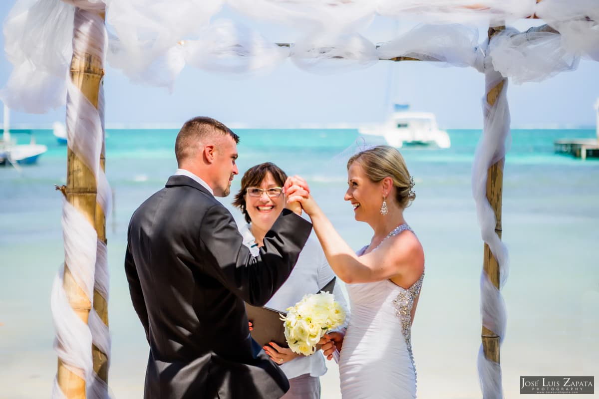 A couple exchanges vows during a beach wedding ceremony, with a celebrant smiling in the background.
