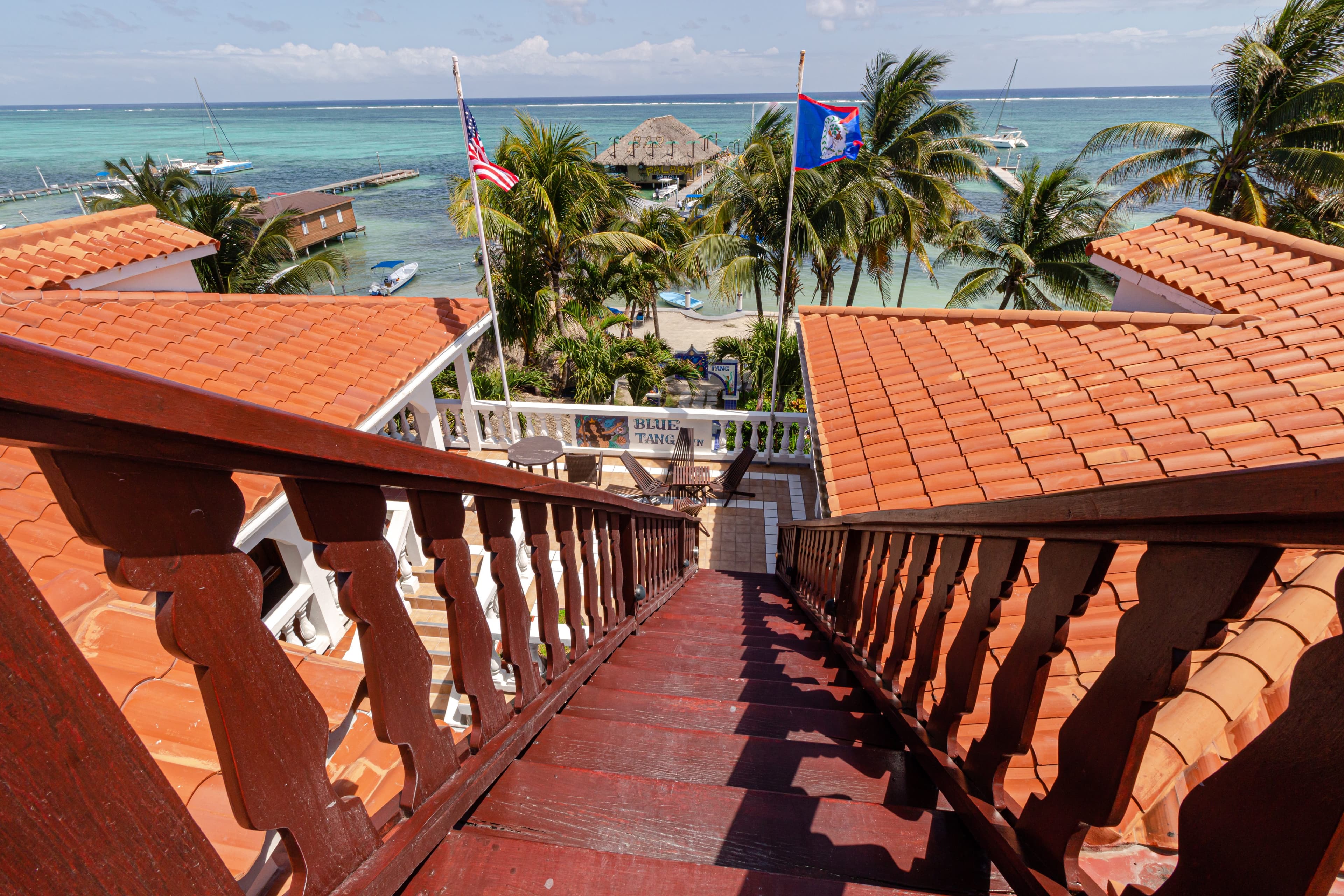 View from a wooden staircase leading down to a tropical beachfront with palm trees and boats.